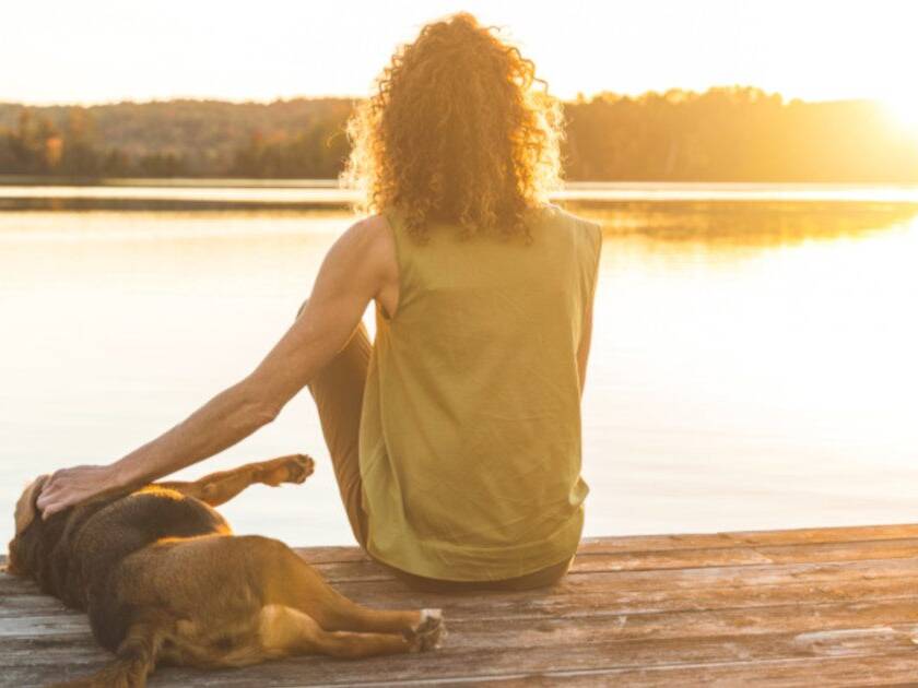 Anxiety and Depression - Lady with her dog sitting by a lake at sunset, the dog laying down next to her with her hand on its back, sharing a peaceful moment.
