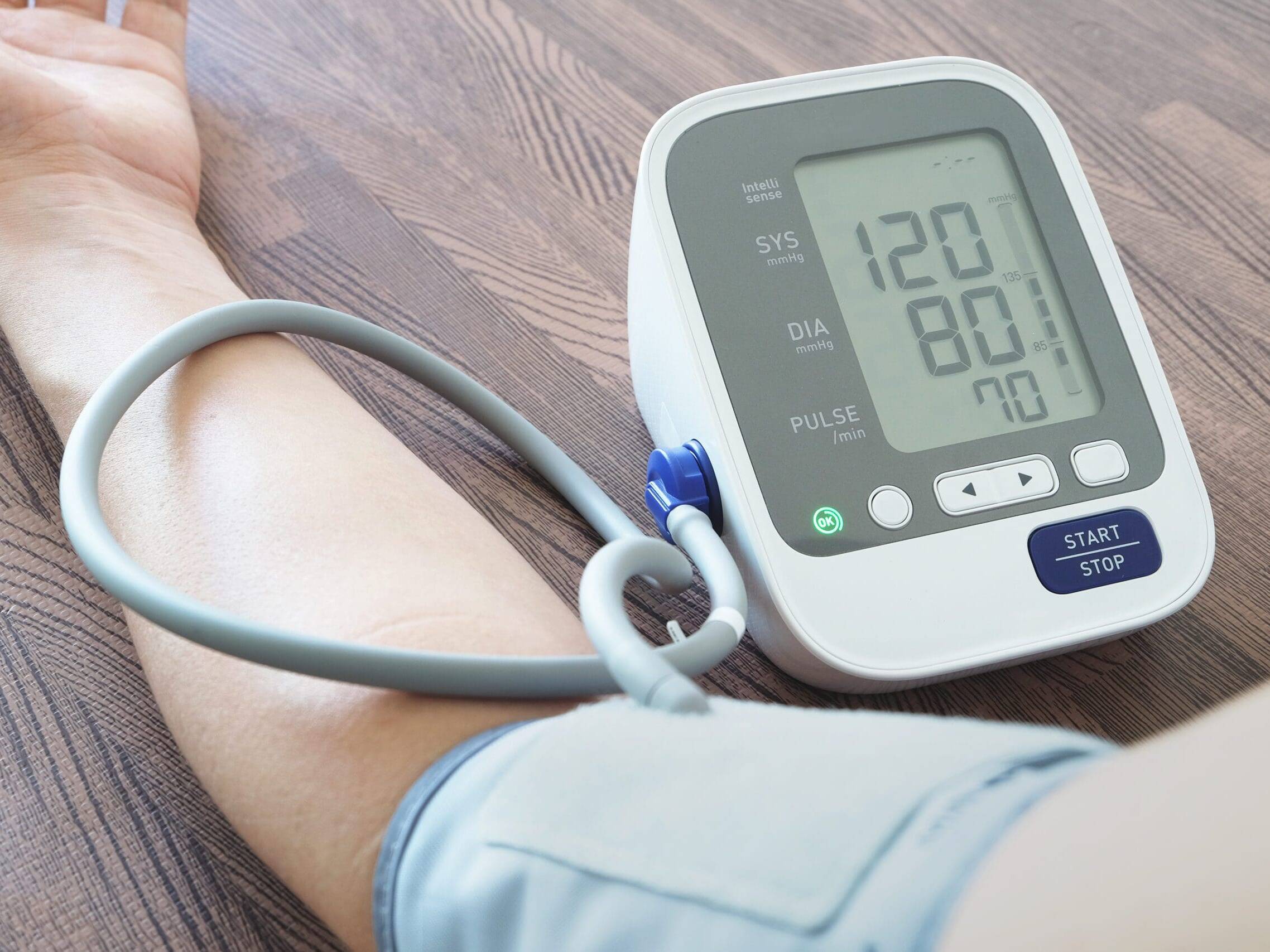 At Home Blood Pressure Monitoring - Close-up of an arm with a digital blood pressure monitor showing 120/80 mmHg.