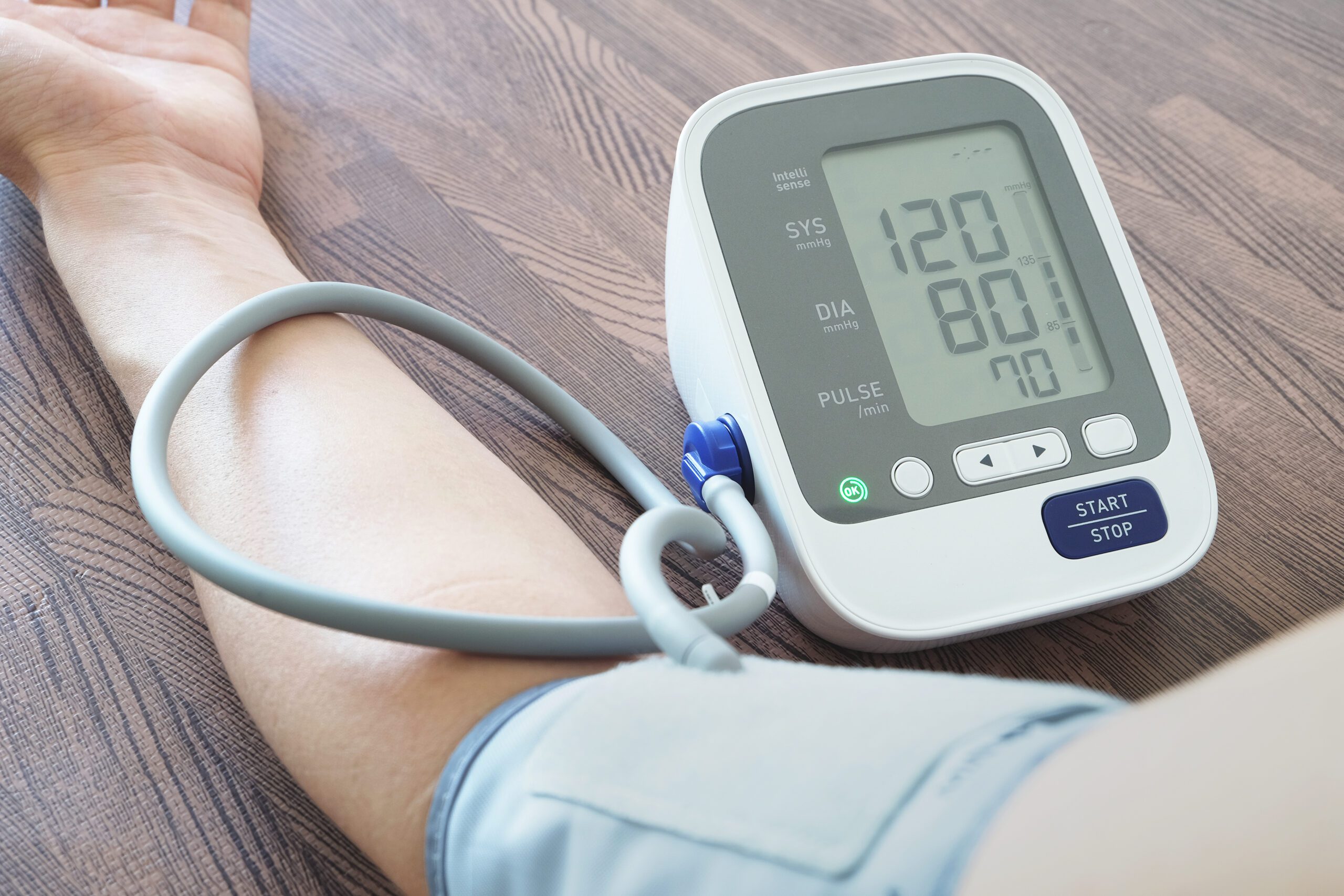 At Home Blood Pressure Monitoring - Close-up of an arm with a digital blood pressure monitor showing 120/80 mmHg.