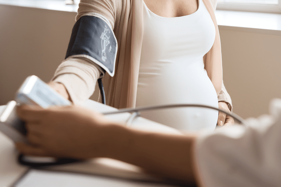 Pregnant woman measuring her blood pressure with a home monitor, highlighting prenatal care after preeclampsia.