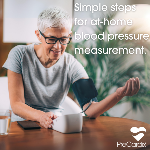 Happy woman checking her blood pressure at home with a digital monitor, a glass of water, and her smartphone on the dining table.