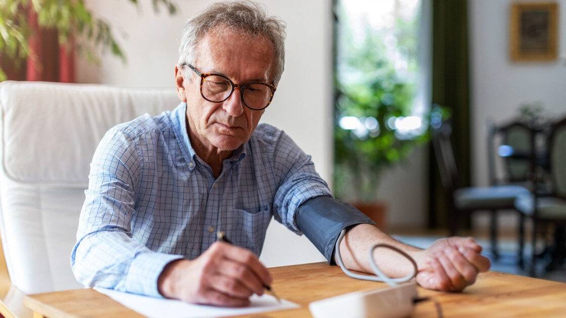 Older man monitoring his blood pressure and diligently noting the results on paper, practicing responsible health management.
