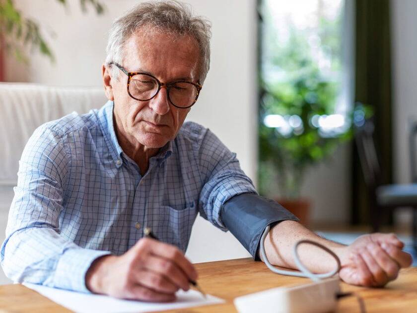 Older man monitoring his blood pressure and diligently noting the results on paper, practicing responsible health management.