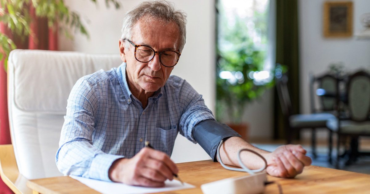 Older man monitoring his blood pressure and diligently noting the results on paper, practicing responsible health management.