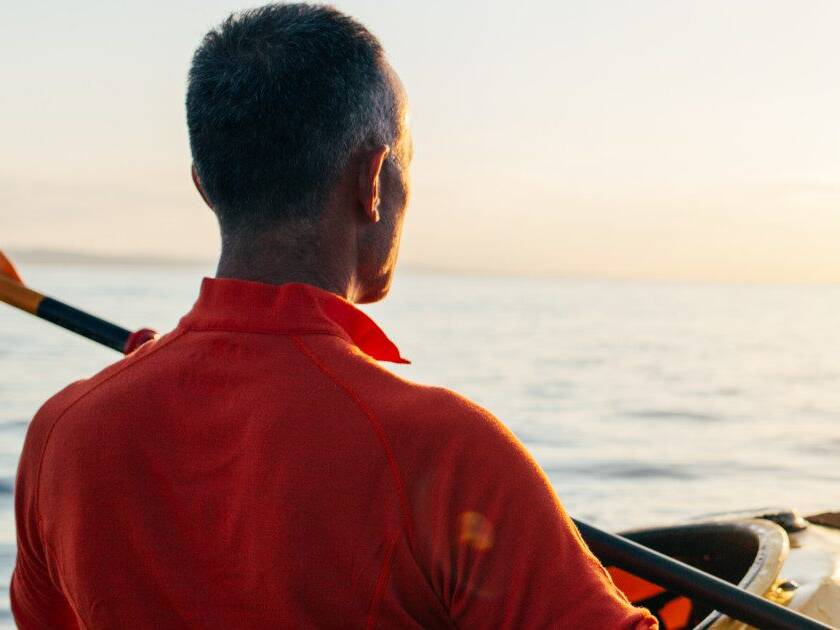 Man kayaking in calm waters against a stunning sunset, symbolizing stress relief and the link to maintaining healthy blood pressure.