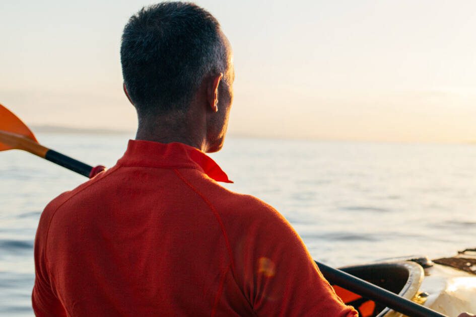 Man kayaking in calm waters against a stunning sunset, symbolizing stress relief and the link to maintaining healthy blood pressure.