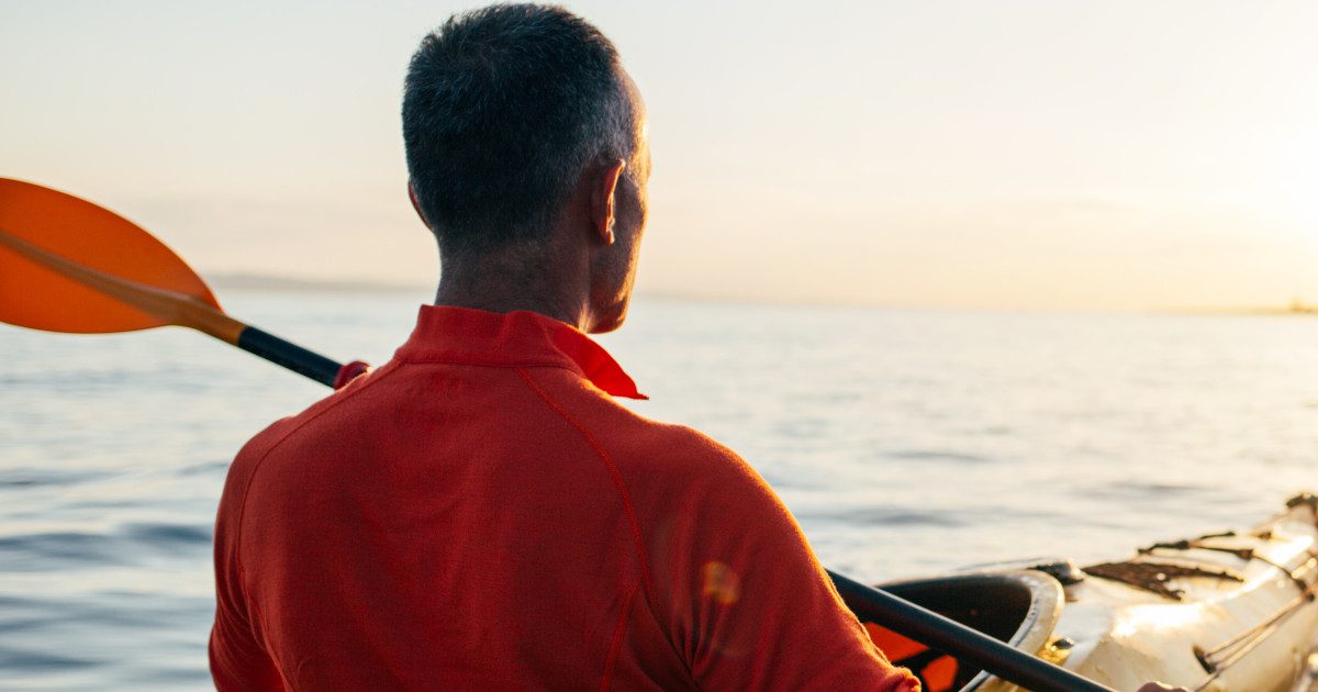 Man kayaking in calm waters against a stunning sunset, symbolizing stress relief and the link to maintaining healthy blood pressure.
