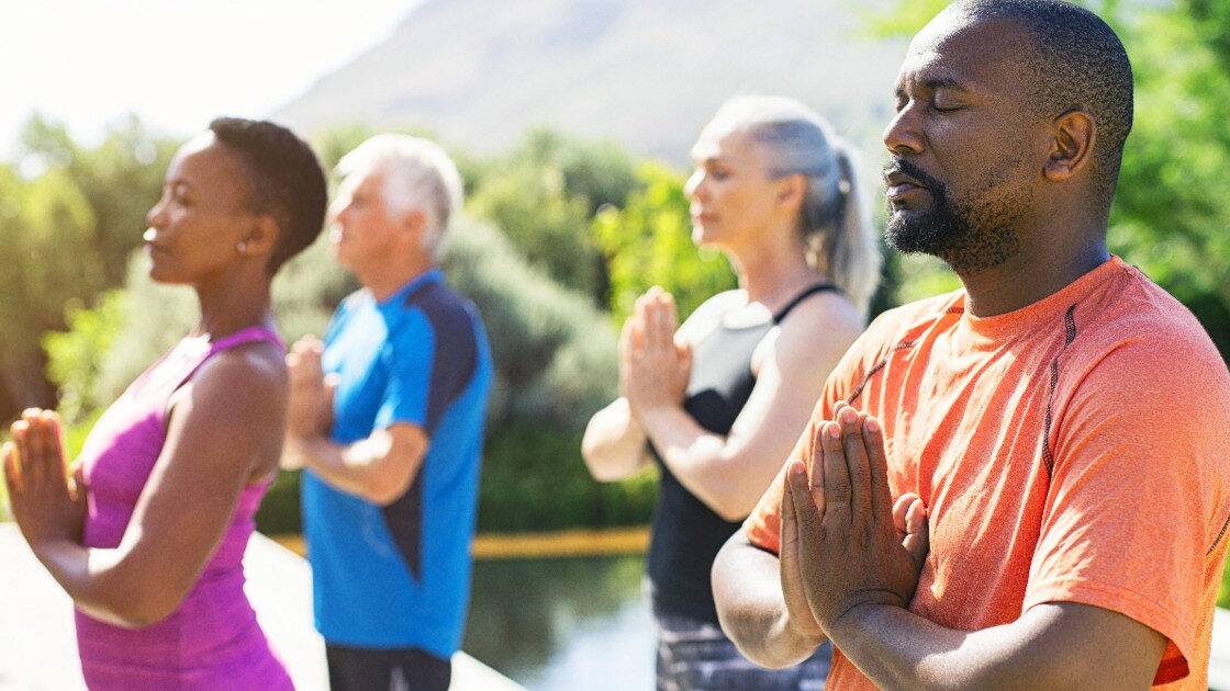 Group practicing breath-focused meditation outdoors for blood pressure control, embodying tranquility and collective wellness in serene weather.