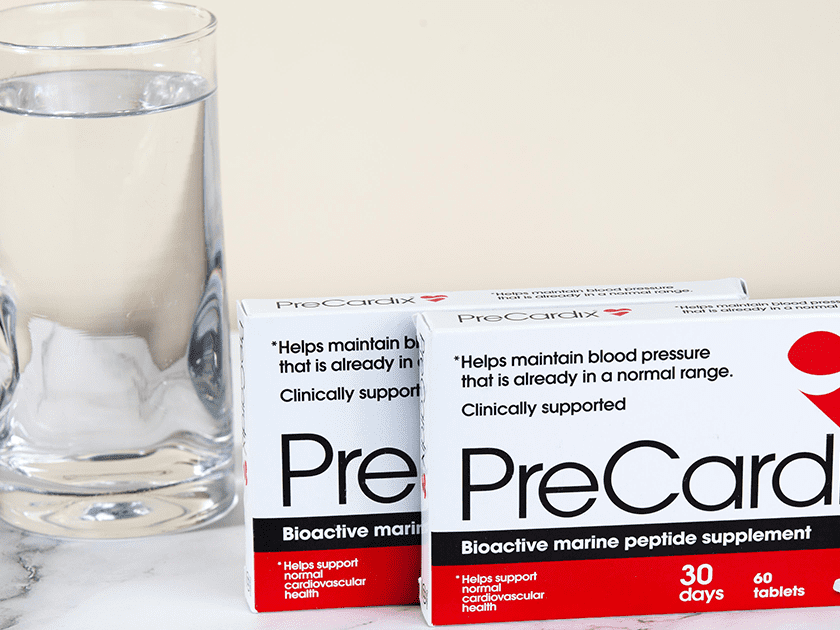 Heart Hydration: A PreCardix® package box next to a clear glass of water, placed on a marble table indoors.