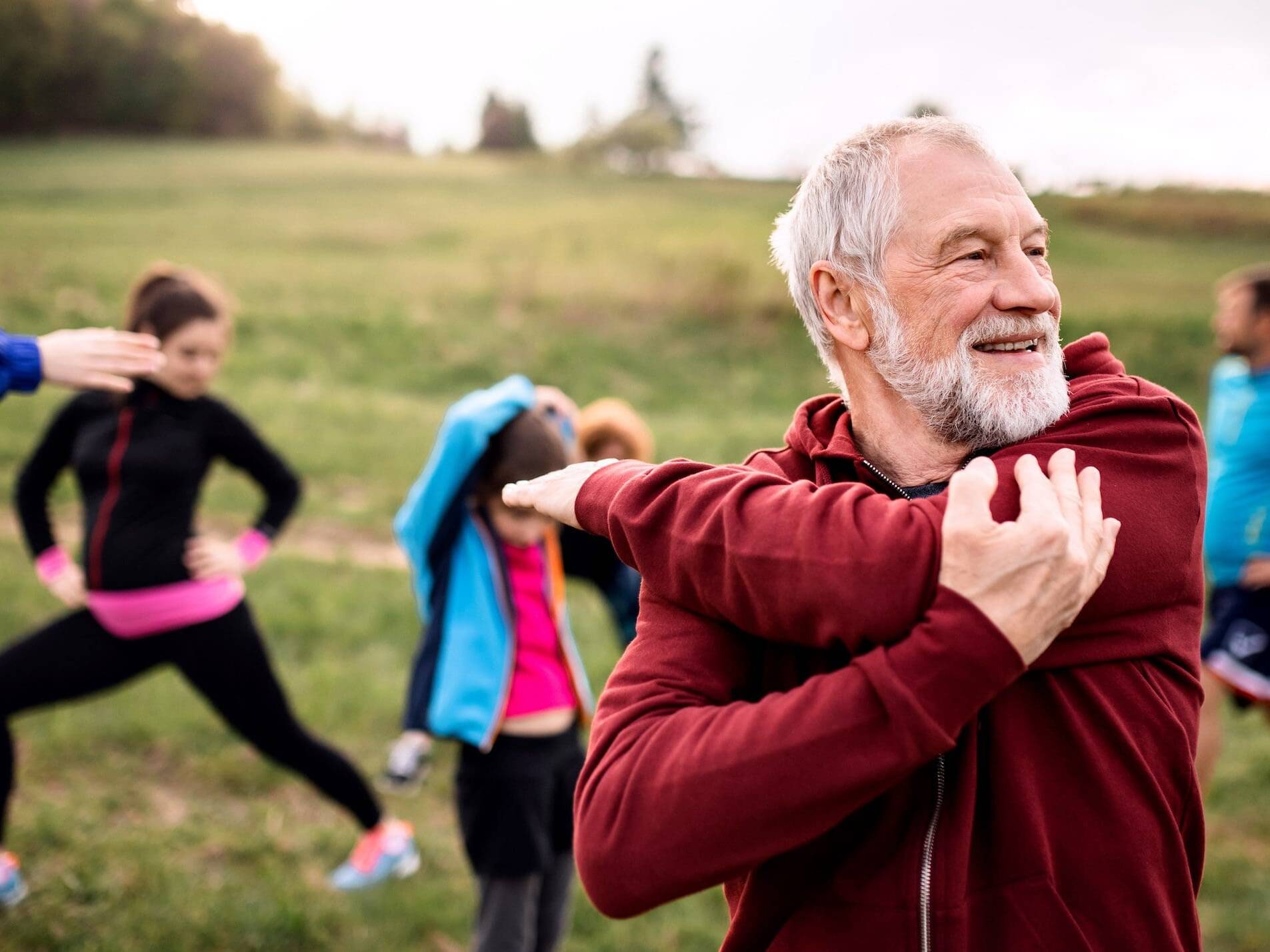 Large group of active individuals stretching outdoors, embodying heart health through exercise in nature.