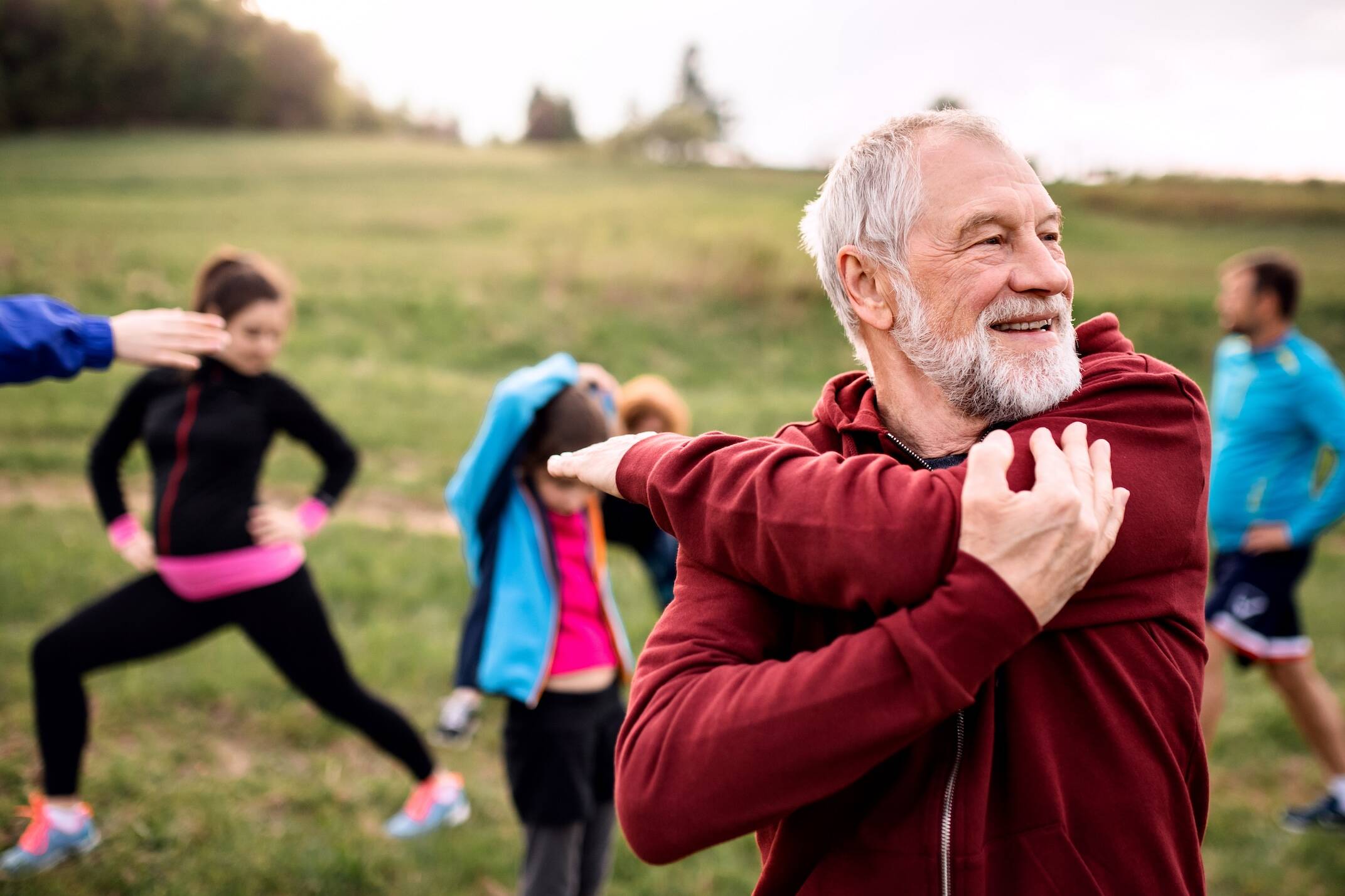 Large group of active individuals stretching outdoors, embodying heart health through exercise in nature.