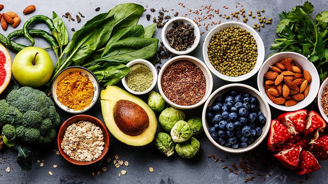 Heart Healthy Cooking: Close-up of a variety of heart-healthy foods, including avocado, berries, green apple, spinach, nuts, seasoning powder, peppers, broccoli, and Brussels sprouts.