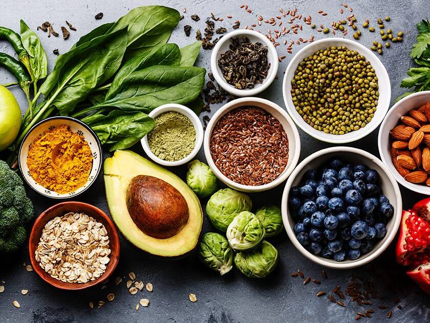 Heart Healthy Cooking: Close-up of a variety of heart-healthy foods, including avocado, berries, green apple, spinach, nuts, seasoning powder, peppers, broccoli, and Brussels sprouts.