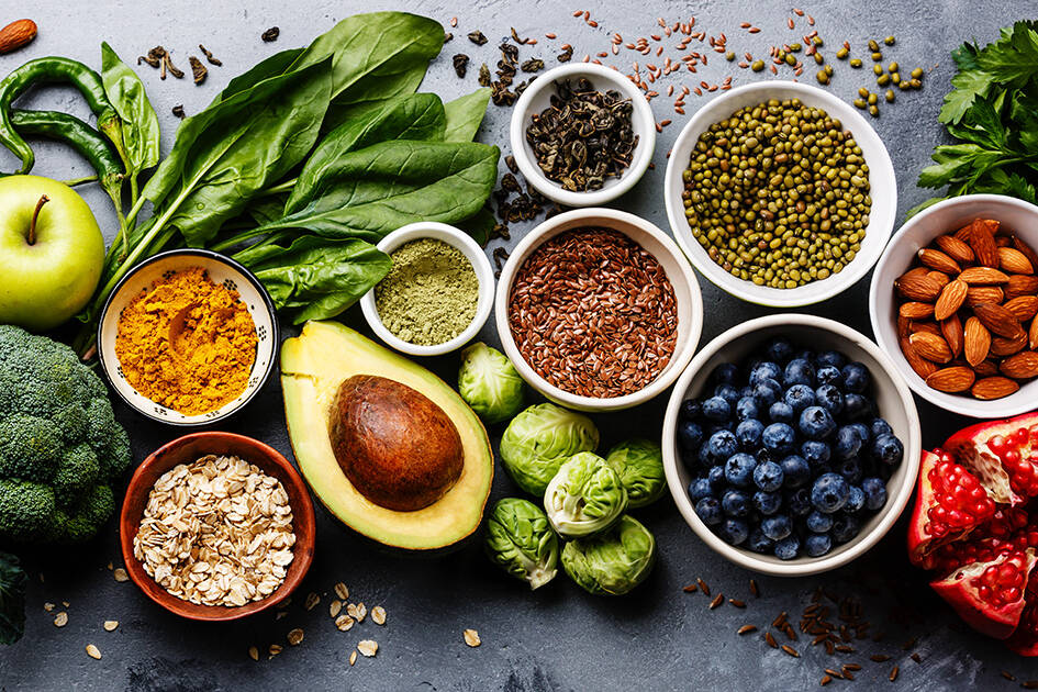 Heart Healthy Cooking: Close-up of a variety of heart-healthy foods, including avocado, berries, green apple, spinach, nuts, seasoning powder, peppers, broccoli, and Brussels sprouts.