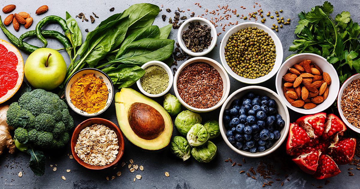 Heart Healthy Cooking: Close-up of a variety of heart-healthy foods, including avocado, berries, green apple, spinach, nuts, seasoning powder, peppers, broccoli, and Brussels sprouts.