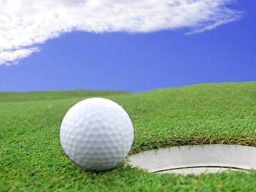 Eco-Friendly Lifestyle: Close-up of a golf ball on a golf course, embodying an eco-friendly lifestyle choice, under clear skies with light clouds.