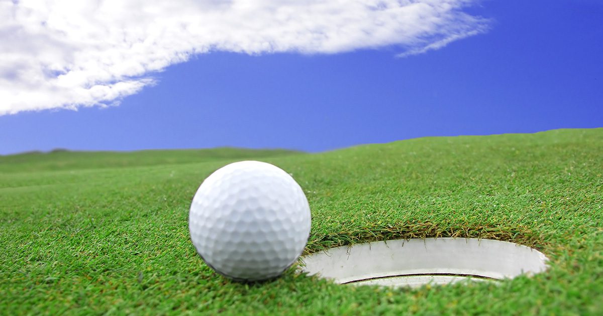 Eco-Friendly Lifestyle: Close-up of a golf ball on a golf course, embodying an eco-friendly lifestyle choice, under clear skies with light clouds.