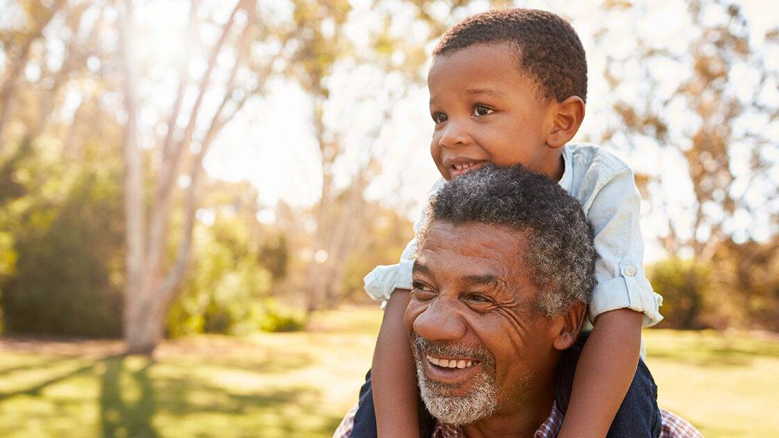 Genetics and Heart Health: Grandpa holding his grandson on his shoulders at a park during the evening.