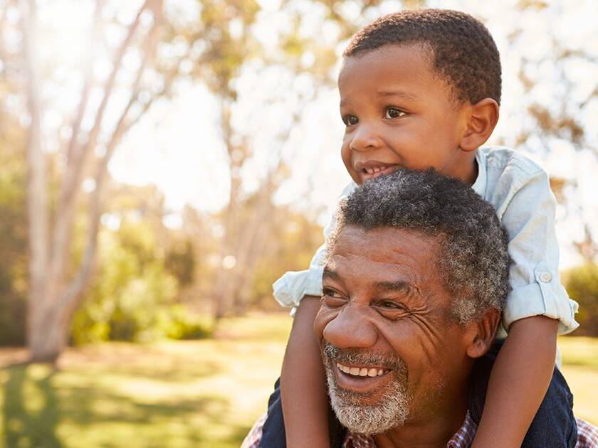 Genetics and Heart Health: Grandpa holding his grandson on his shoulders at a park during the evening.