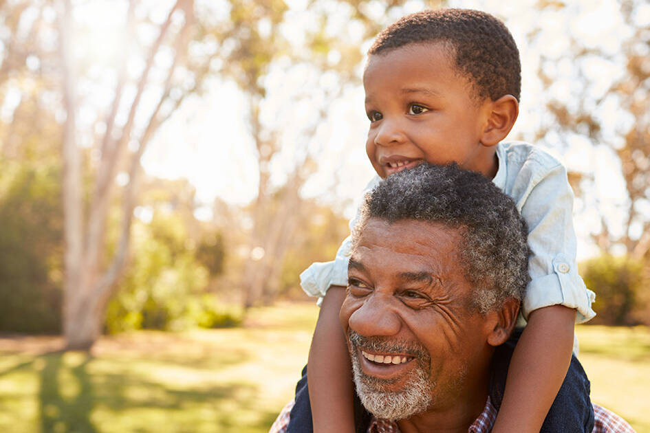 Genetics and Heart Health: Grandpa holding his grandson on his shoulders at a park during the evening.