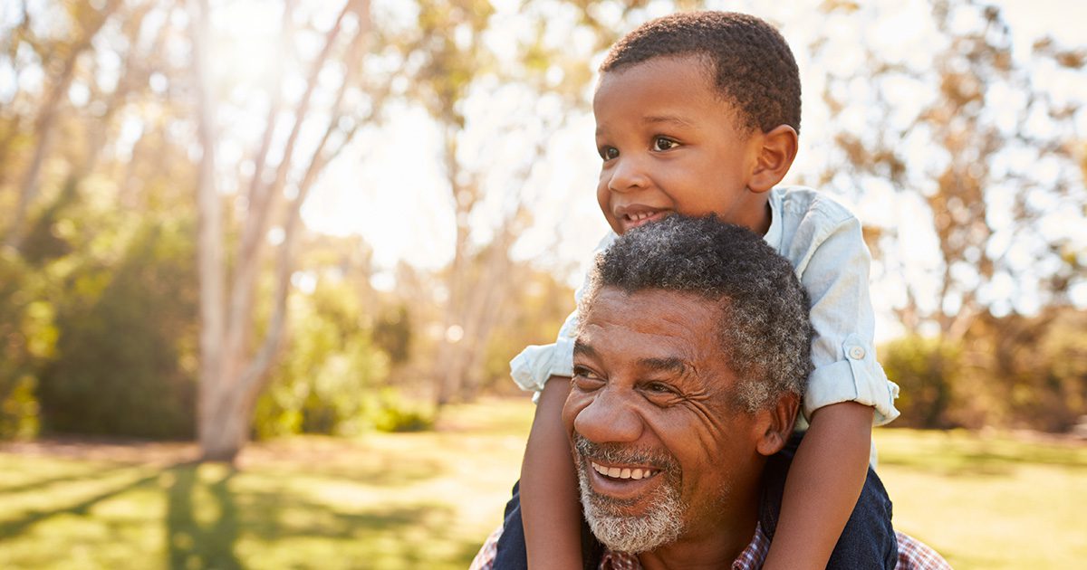Genetics and Heart Health: Grandpa holding his grandson on his shoulders at a park during the evening.